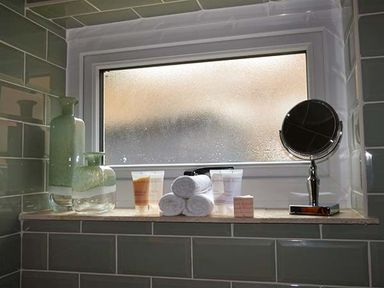 A bathroom window sill with rolled towels toiletries glass bottles and a round mirror at Kitts Cottage in Little Malvern near Malvern
