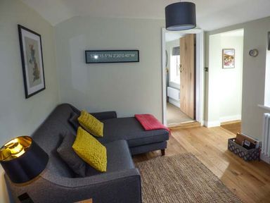 A living room with a gray sofa with yellow cushions a black lamp a rug and wooden floor at Kitts Cottage in Little Malvern near Malvern