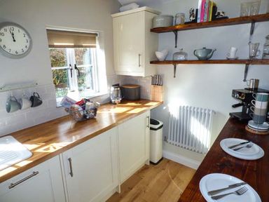 A kitchen with wooden countertops cups on hooks and plates on a wooden table at Kitts Cottage in Little Malvern near Malvern