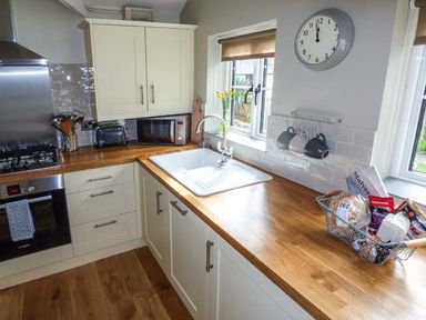 A kitchen with white cabinets a wooden countertop a sink a microwave and a basket of groceries at Kitts Cottage in Little Malvern near Malvern