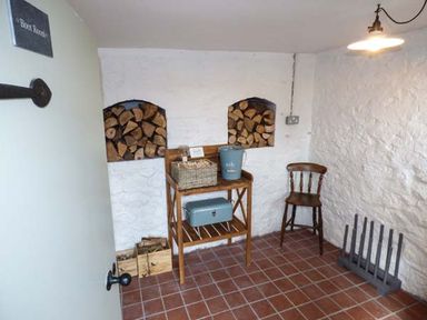 A boot room with a wooden chair a shelf unit with storage boxes and firewood in wall niches at Kitts Cottage in Little Malvern near Malvern
