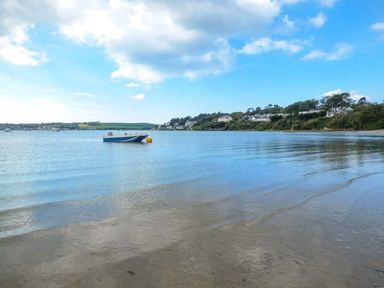 A view of a calm beach with a small boat floating on water and houses on the shoreline at Kilcarreg Rock near Wadebridge