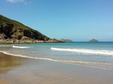 A beach with gentle waves and rocky hills on the left side at Kilcarreg Rock near Wadebridge