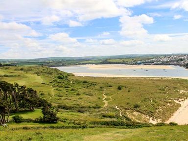 A coastal landscape with grassy hills trees a sandy beach and a town in the distance at Kilcarreg Rock near Wadebridge