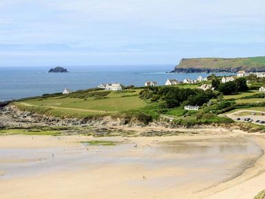 A coastal landscape with sandy beach grassy fields white houses and cliffs at Kilcarreg Rock near Wadebridge