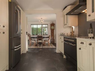 A kitchen with a black refrigerator and stove leading to a dining area with a wooden table chairs and a grandfather clock at Kilcarreg Rock near Wadebridge