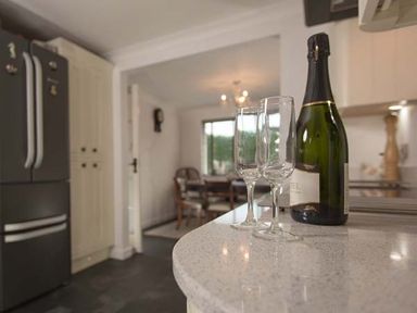 A kitchen counter with two empty glasses and a bottle of champagne a dining area with chairs in the background at Kilcarreg Rock near Wadebridge