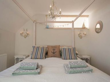 A bedroom with a four-poster bed and striped pillows with blankets folded on top at Kilcarreg in Rock near Wadebridge