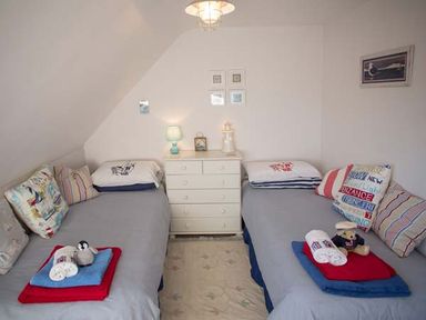 A bedroom with two single beds separated by a white chest of drawers with a lamp and decorations at Kilcarreg Rock near Wadebridge