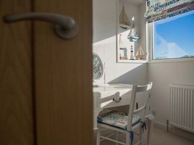 A small white desk and chair with a cushioned seat near a window with nautical decorations at Kilcarreg Rock near Wadebridge