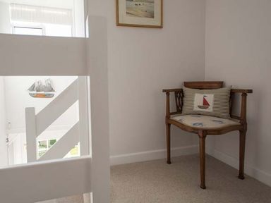 A wooden corner chair with a cushion featuring a sailboat in a white room near a staircase at Kilcarreg in Rock near Wadebridge