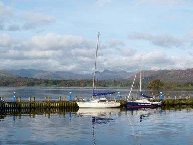 A lake with two sailboats moored at a wooden dock with hills in the background at The Oaks in Bowness Windermere