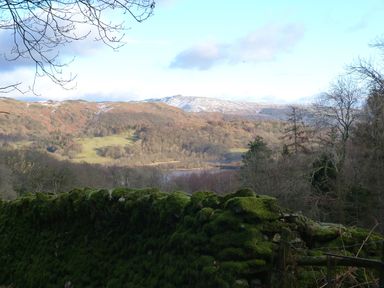 A landscape with moss-covered stone wall in foreground and hills with sparse trees and patches of snow in background at The Oaks in Bowness & Windermere