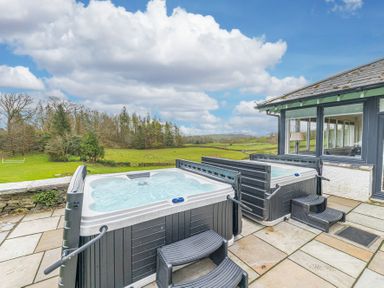 An outdoor patio with two hot tubs and steps overlooking a grassy field and trees at The Oaks in Bowness Windermere