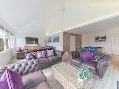A living room with brown leather sofas purple cushions a wicker coffee table a flat screen tv and a pool table at The Oaks in Bowness & Windermere