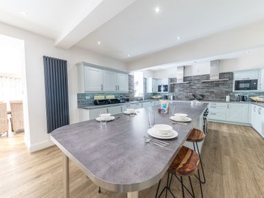 A modern kitchen with a large island counter set with plates and glasses at The Oaks in Bowness & Windermere