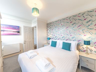 A bedroom with a bed two teal pillows two bedside tables with lamps and a door at The Oaks in Bowness & Windermere