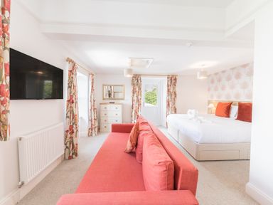 A bedroom with a red sofa a bed with red pillows floral curtains and a wall-mounted TV at The Oaks in Bowness & Windermere