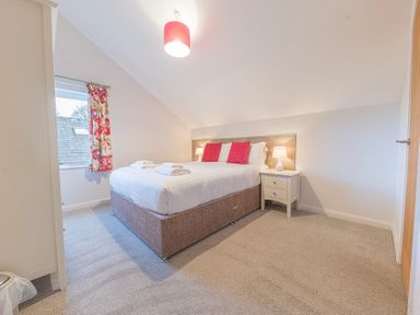 A bedroom with a bed with pink cushions bedside tables and lamps and a window with floral curtains at The Oaks in Bowness Windermere