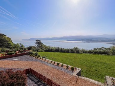 A garden with grass and shrubs overlooking a body of water with hills in the background at Menai View near Menai Bridge