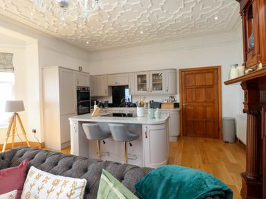 A kitchen with an island and two stools a wooden door and a sofa with pillows at Menai View near Menai Bridge