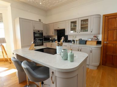 A kitchen with an island countertop with utensils and chairs near a wooden door at Menai View near Menai Bridge