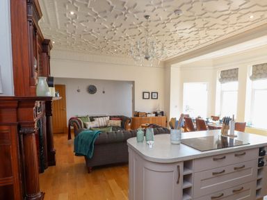 An open living and dining area with a kitchen island and a wooden fireplace at Menai View near Menai Bridge