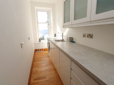 A narrow kitchen with wooden floor and white cabinets near a window at Menai View near Menai Bridge