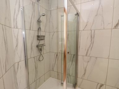A shower area with marble patterned tiles and a glass door at Menai View near Menai Bridge