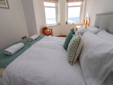 A bed with pillows and rolled towels near two windows and a wooden chair at Menai View near Menai Bridge