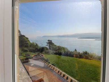 A view of a grassy garden and trees overlooking a large body of water and distant hills near Menai Bridge