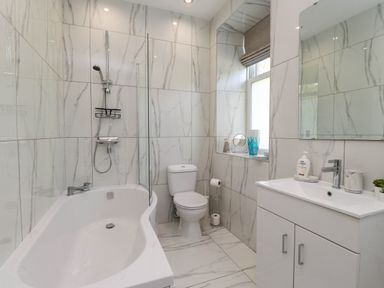 A bathroom with a bathtub shower combination a toilet and a sink with cabinet at Menai View near Menai Bridge