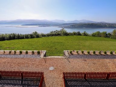 A garden with green grass and small plants overlooking a body of water with mountains in the background at Menai View near Menai Bridge
