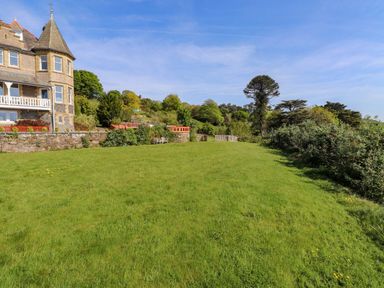 A large grassy garden area with benches and trees beside a stone building at Menai View near Menai Bridge
