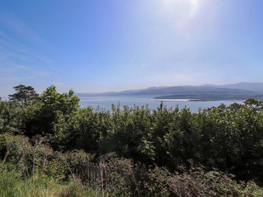 A view of a body of water with hills in the background and bushes in the foreground at Menai View near Menai Bridge