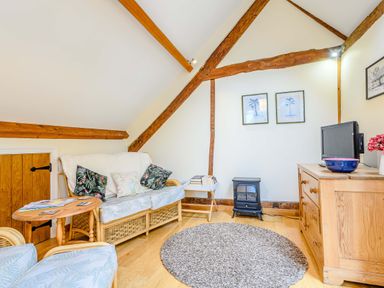 A living room with wicker furniture a small wooden table a gray round rug a wooden dresser with a TV and two framed pictures on the wall at The Bothy in Phocle Green near Ross-on-Wye
