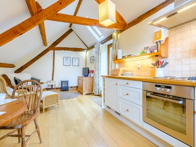 A kitchen and living area with wooden beams dining table and chairs a sofa and a stove at The Bothy Phocle Green near Ross-on-Wye