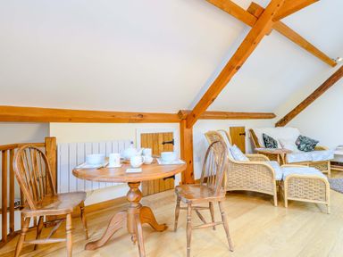 A dining area with a round wooden table set for tea and two wooden chairs next to a seating area with wicker furniture at The Bothy in Phocle Green near Ross-on-Wye