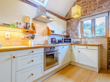 A kitchen with white cabinets wooden countertops a stove oven microwave and a window at The Bothy Phocle Green near Ross-on-Wye