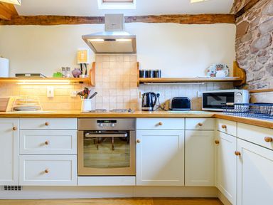 A kitchen with white cabinets a stainless steel oven electric stove kettle toaster microwave and wooden countertops at The Bothy in Phocle Green near Ross-on-Wye