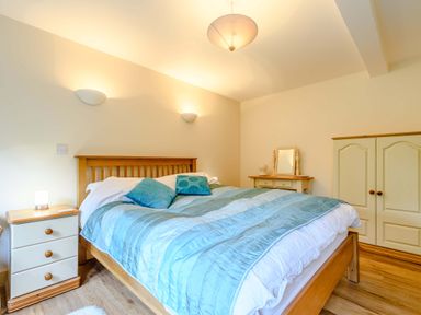 A bedroom with a wooden bed a blue comforter bedside table and wardrobe at The Bothy Phocle Green near Ross-on-Wye