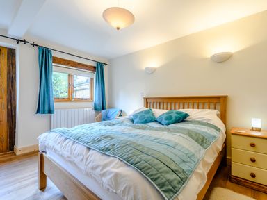 A bedroom with a wooden bed and blue bedding near a window with blue curtains at The Bothy in Phocle Green near Ross-on-Wye