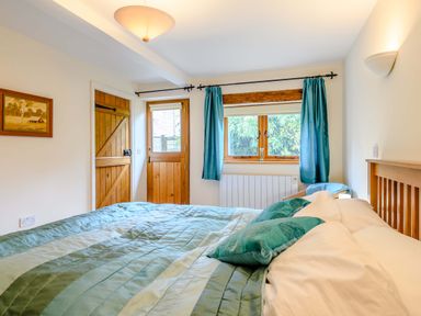 A bedroom with a bed a wooden door a window with blue curtains and a framed picture on the wall at The Bothy in Phocle Green near Ross-on-Wye