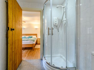 A bathroom with a corner shower cubicle and an open wooden door leading to a bedroom at The Bothy in Phocle Green near Ross-on-Wye
