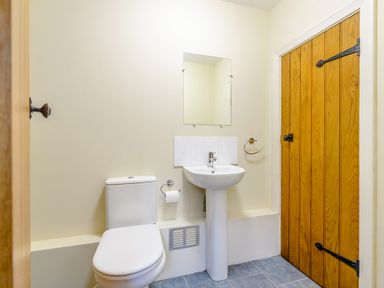 A bathroom with a toilet sink mirror and a wooden door at The Bothy in Phocle Green near Ross-on-Wye