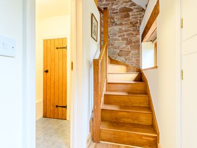 A wooden staircase with a stone wall beside it and a wooden door visible through an open doorway at The Bothy in Phocle Green near Ross-on-Wye