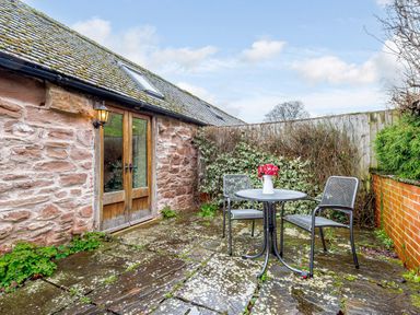 A stone patio with a metal table and two chairs and flowers on the table at The Bothy in Phocle Green near Ross-on-Wye