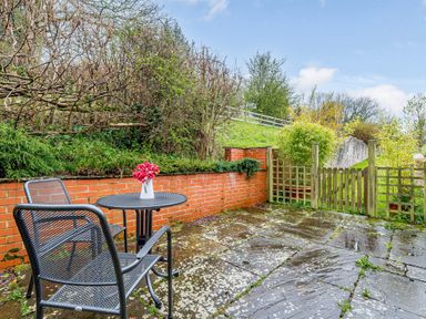 A patio with a small metal table and two chairs with flowers on the table and a wooden gate leading to a garden at The Bothy in Phocle Green near Ross-on-Wye