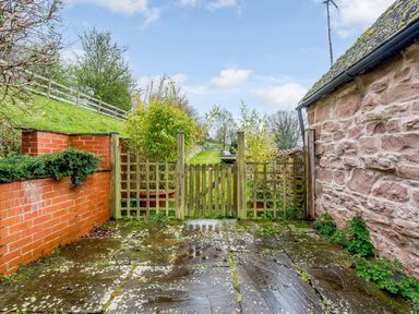 A small fenced garden area with stone pavement and brick and stone walls at The Bothy in Phocle Green near Ross-on-Wye