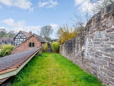 A garden with grass and stone walls near a stone house at The Bothy in Phocle Green near Ross-on-Wye